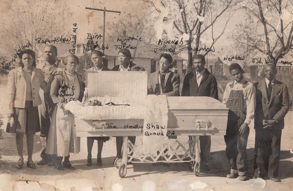 Group of people standing outdoors behind a large hand-painted sign in a sepia-toned historical photo