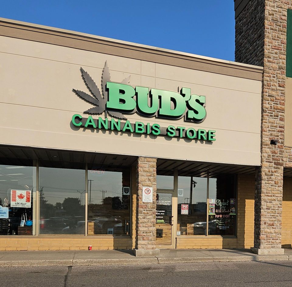 Bud's Cannabis Store, exterior. Green and gray signage, large window, tan building.