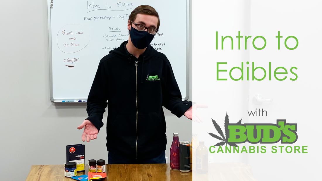 A man in a mask stands behind a table with cannabis edibles, 