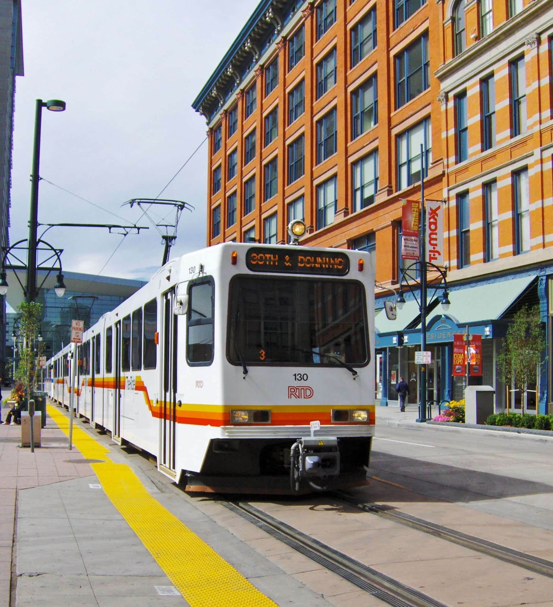 White tram on tracks beside a brick city street with orange buildings and a yellow tactile curb lane