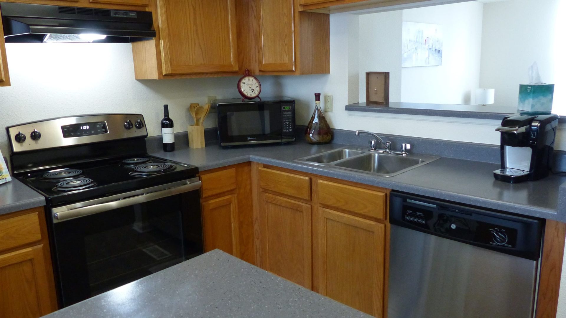 Small kitchen with black stove, wooden cabinets, stainless dishwasher, and a counter under a window.