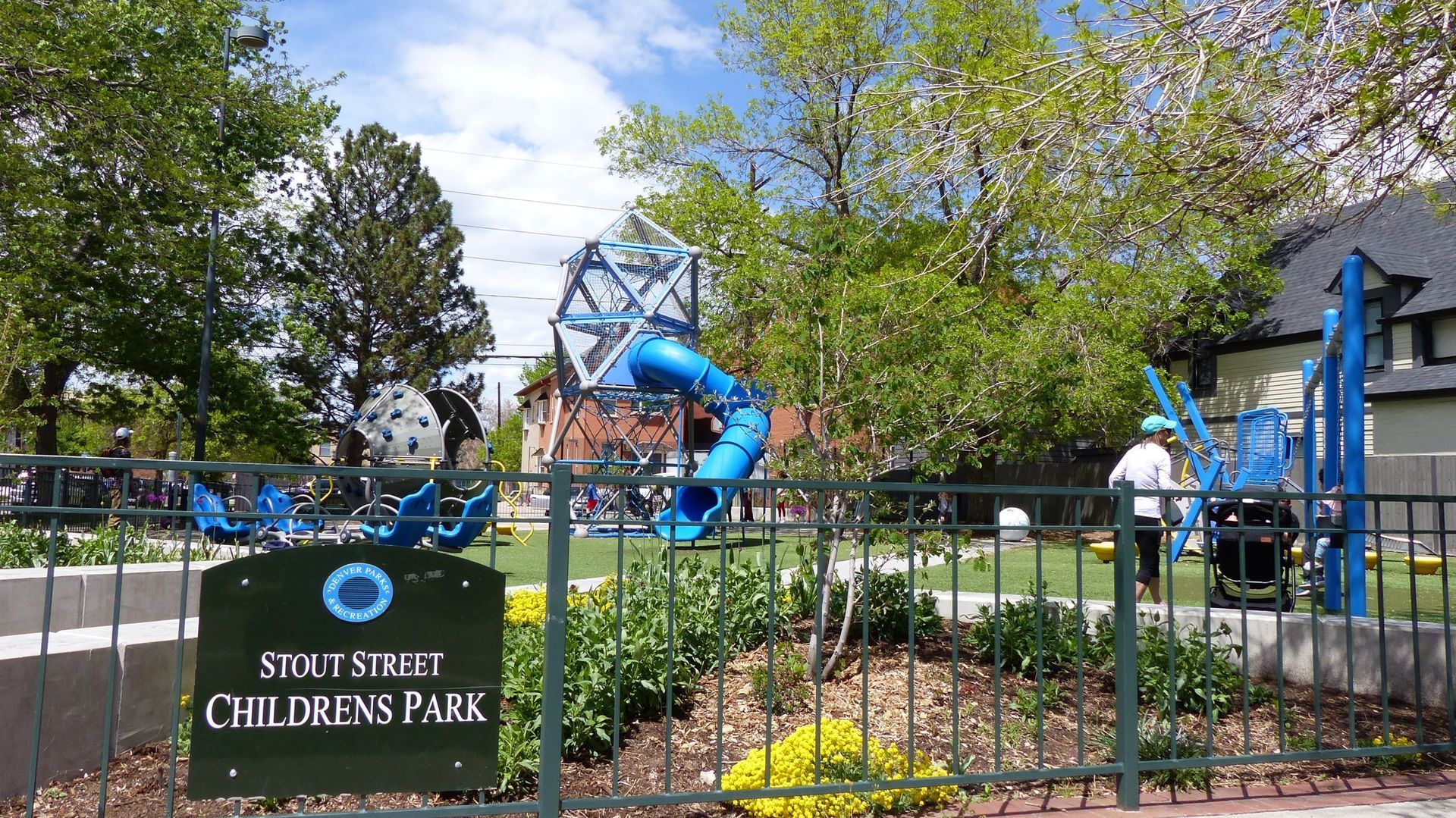 St. Louis Children's Park playground with blue climbing structure, swings, and trees behind a fence