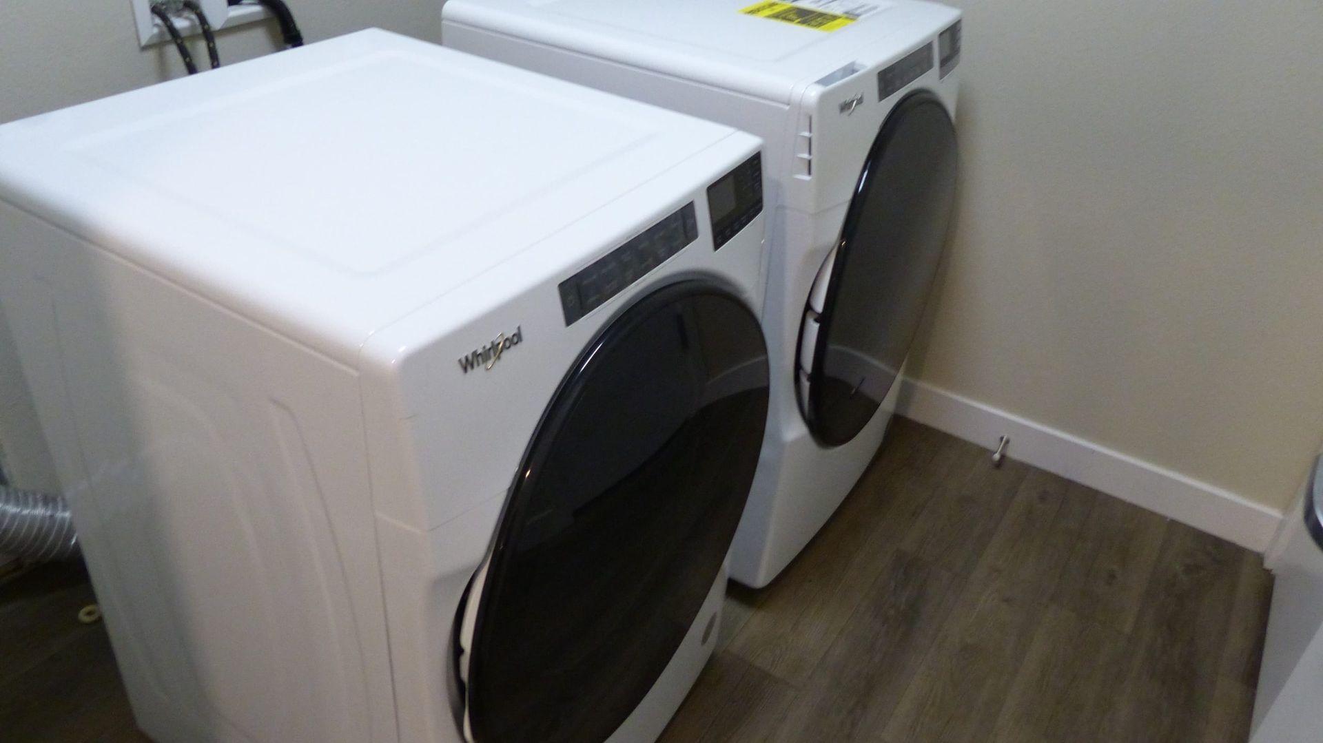 White front-loading washer and dryer in a laundry room corner with a wood floor and beige walls