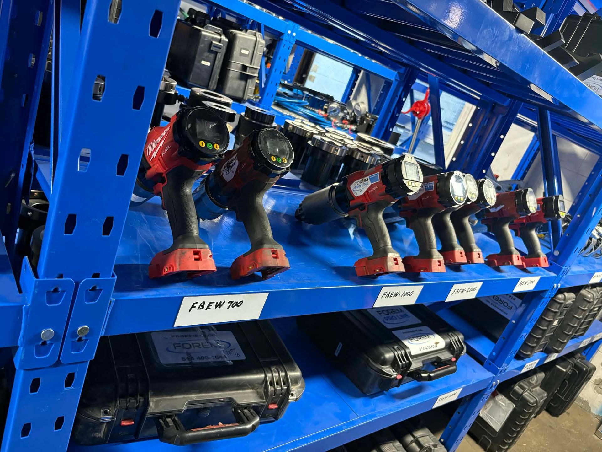 Des étagères bleues contenant de nombreux outils électriques et coffrets rouges et noirs, à l'intérieur d'un entrepôt.