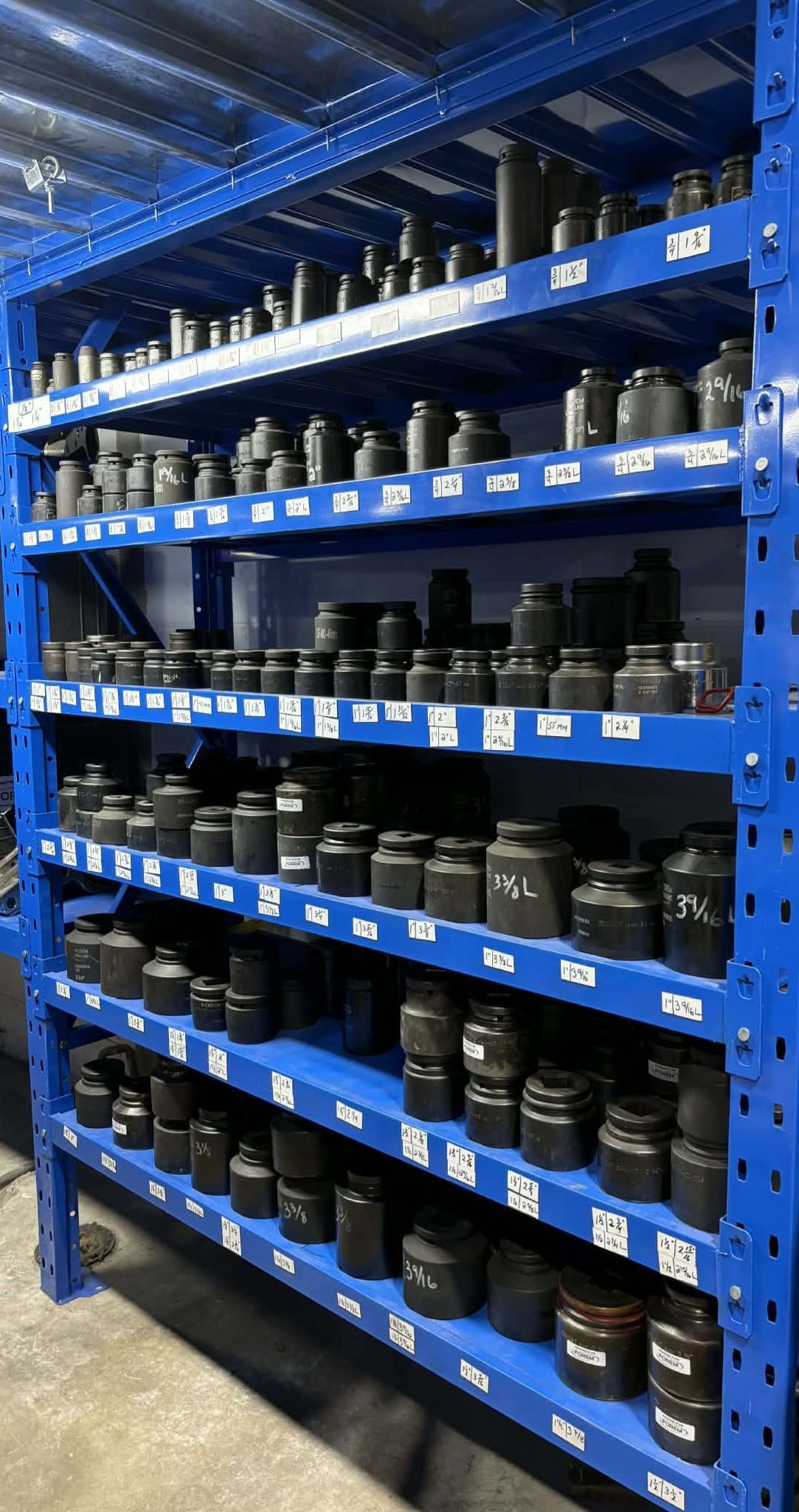 Des étagères métalliques bleues remplies de pièces industrielles noires de différentes tailles.