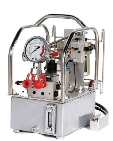 Pompe hydraulique argentée avec manomètre et soupapes à bouchon rouge, logée dans un châssis métallique.