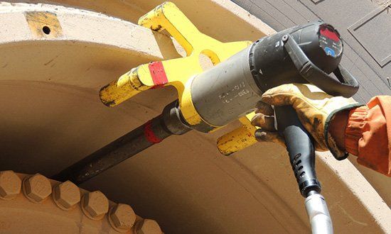 Un ouvrier utilise une clé à chocs jaune pour desserrer les boulons d'une grosse machine.
