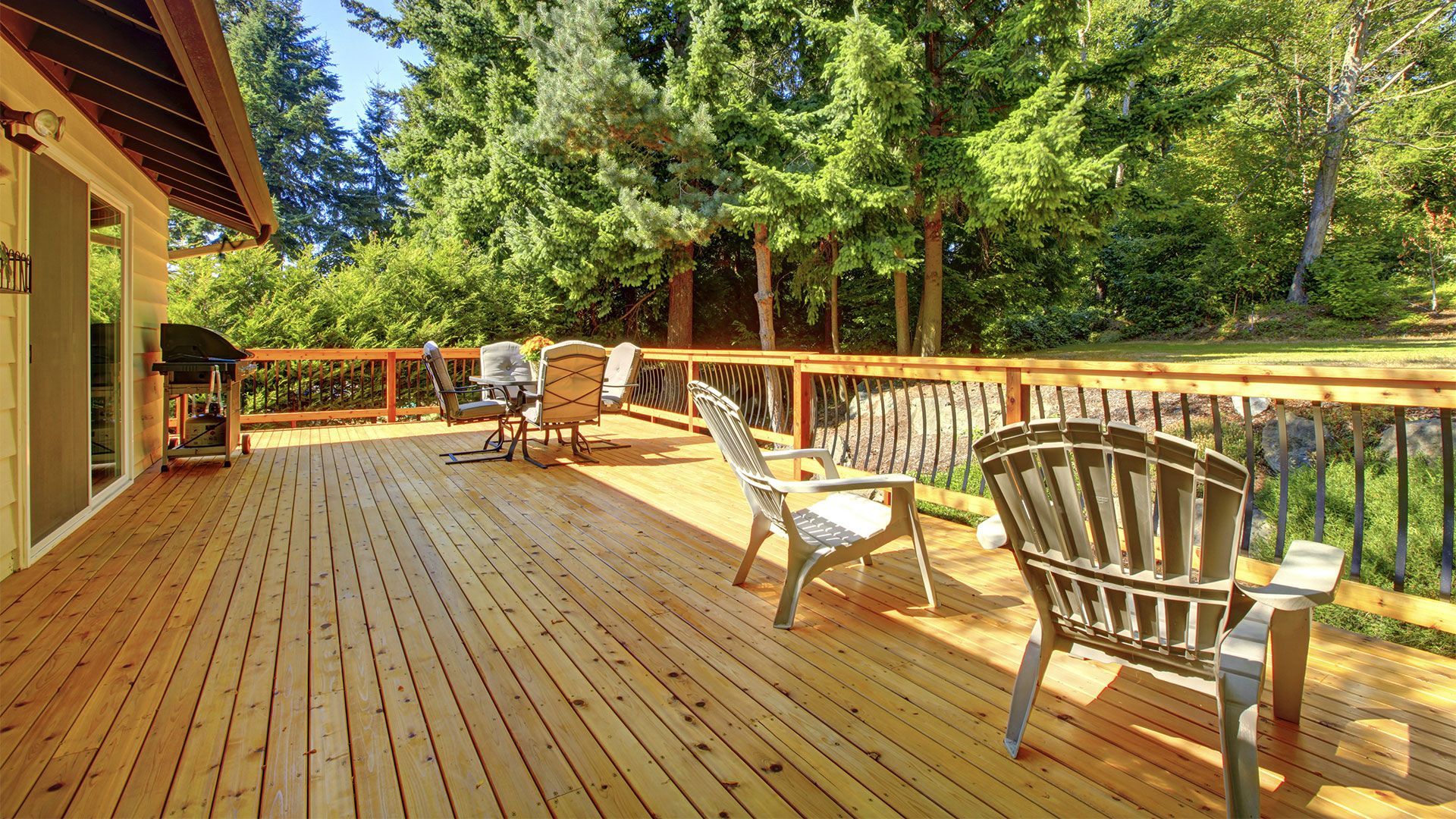 A large wooden deck with chairs and a table surrounded by trees.