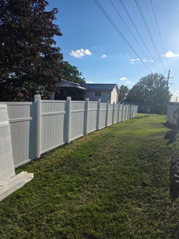 White vinyl fence along a grassy yard under a sunny blue sky, with houses in the background