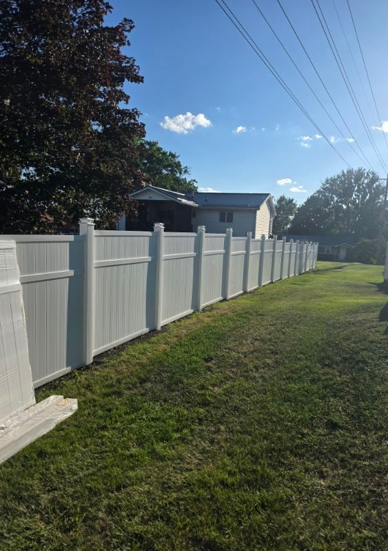 White vinyl fence along a grassy yard beside a house under a blue sky