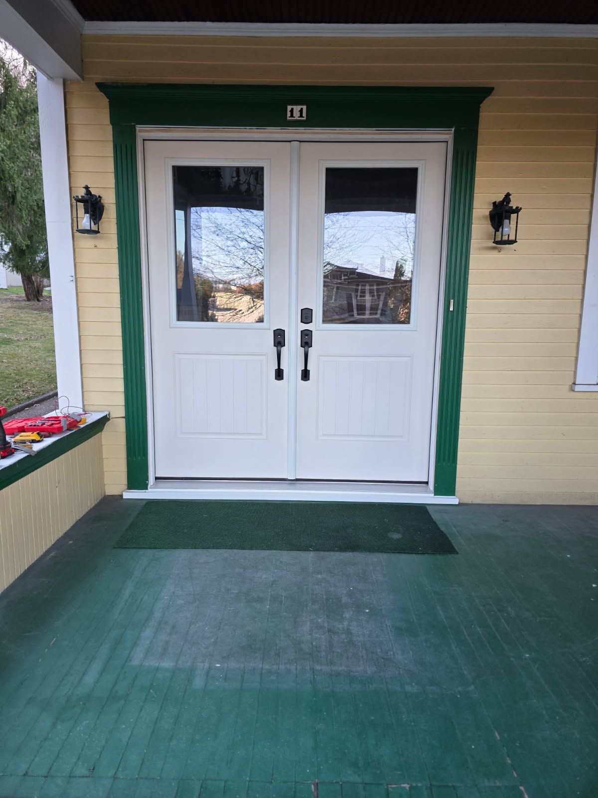 White double front doors with green trim and a dark green porch mat at a house entrance