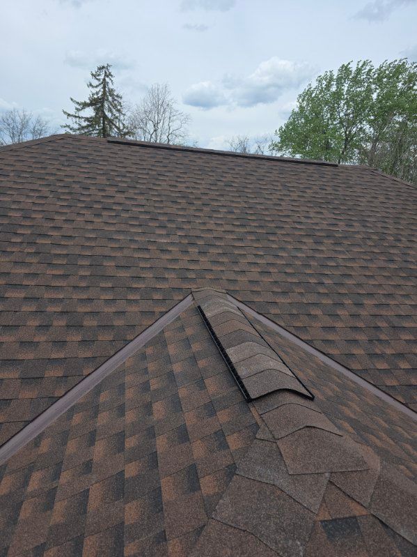 Roof with brown shingles and a damaged ridge vent under a cloudy sky.
