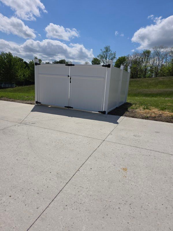 White utility bins on a concrete pad beside a grassy field under a partly cloudy blue sky