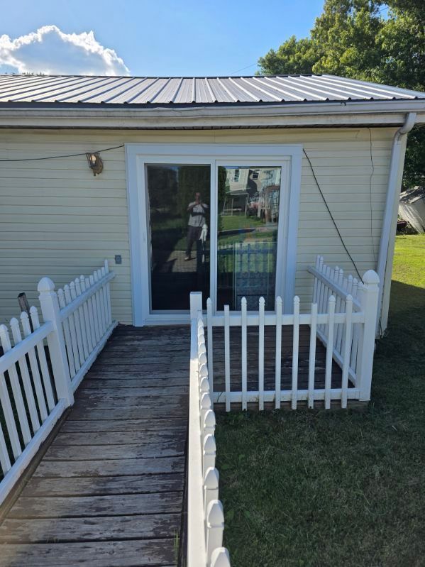 Small white house with a wooden ramp and white picket railings leading to a glass door