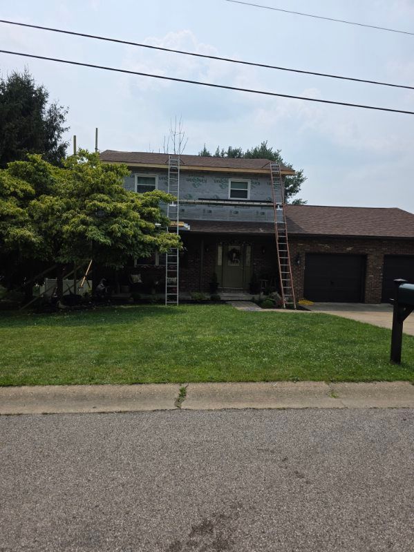 Two-story house with ladders on the front lawn and a garage, viewed from the street under a cloudy sky