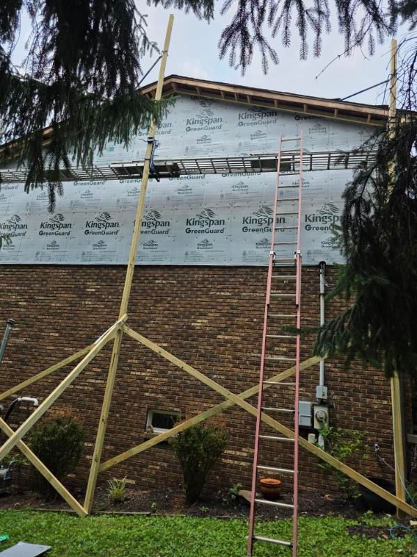Exterior wall under construction with scaffolding and a red ladder, covered in weatherproof sheathing.