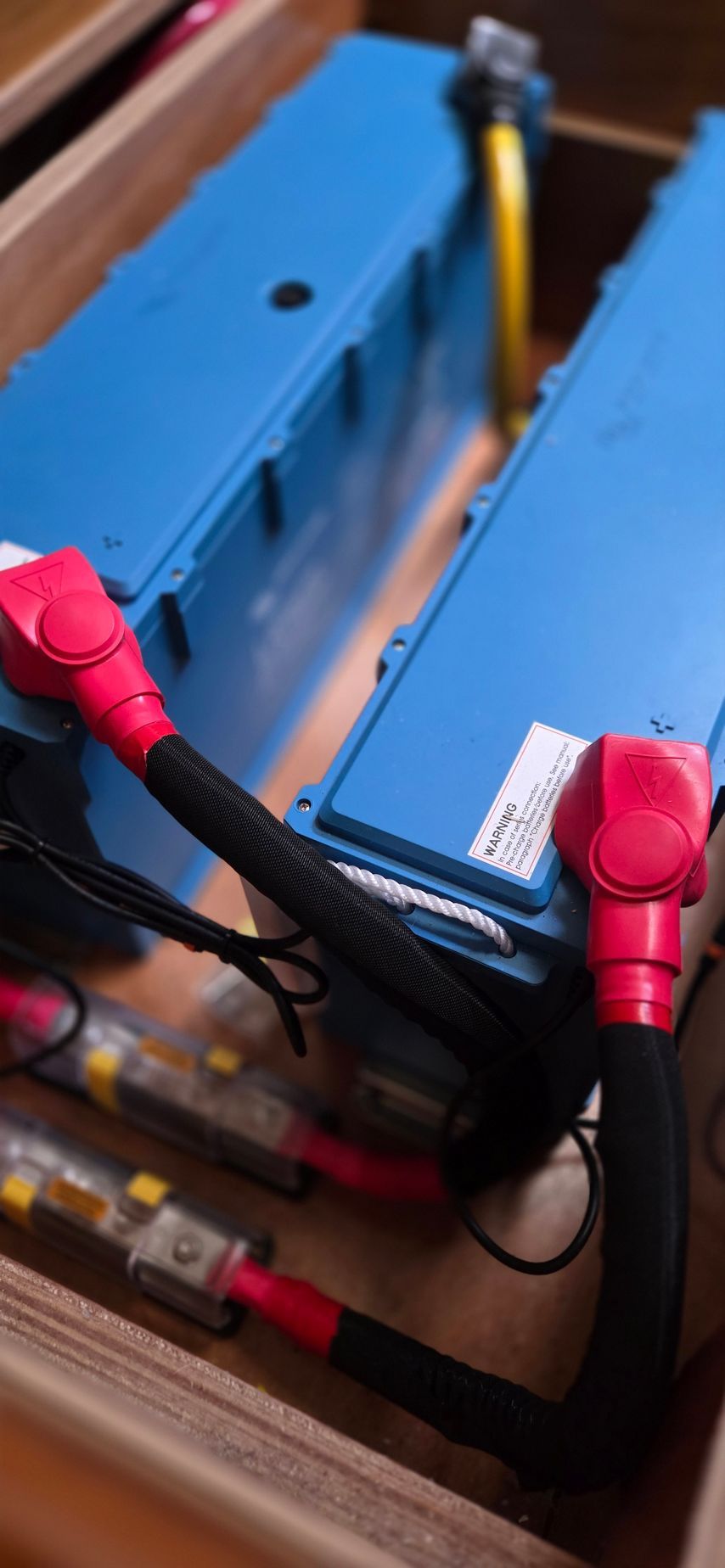 Three blue batteries stacked in a row, connected by thick red power cables secured with white straps.