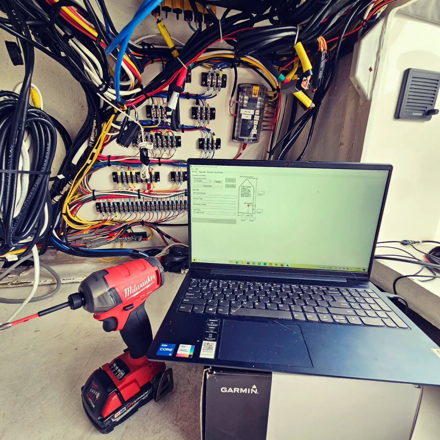 A red power drill and a laptop showing technical wiring diagrams in front of an open marine electrical control panel.