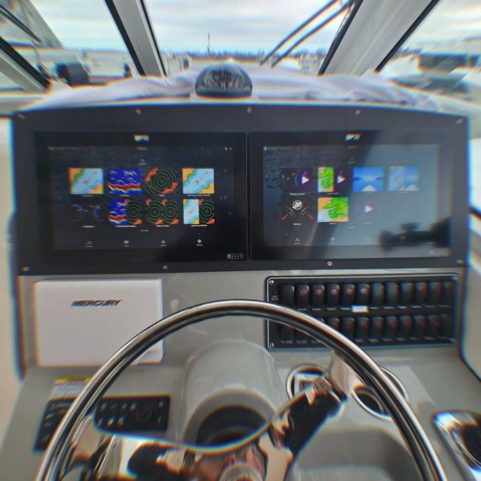 Boat cockpit with dual navigation displays, steering wheel, Mercury instrument panel, and a mounted compass.
