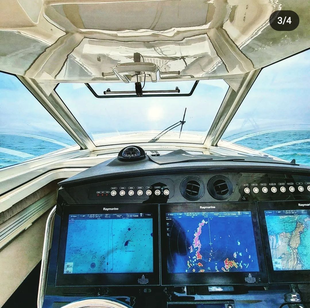 The view from the helm of a boat showing a dashboard with multiple navigation screens looking out over the open sea.