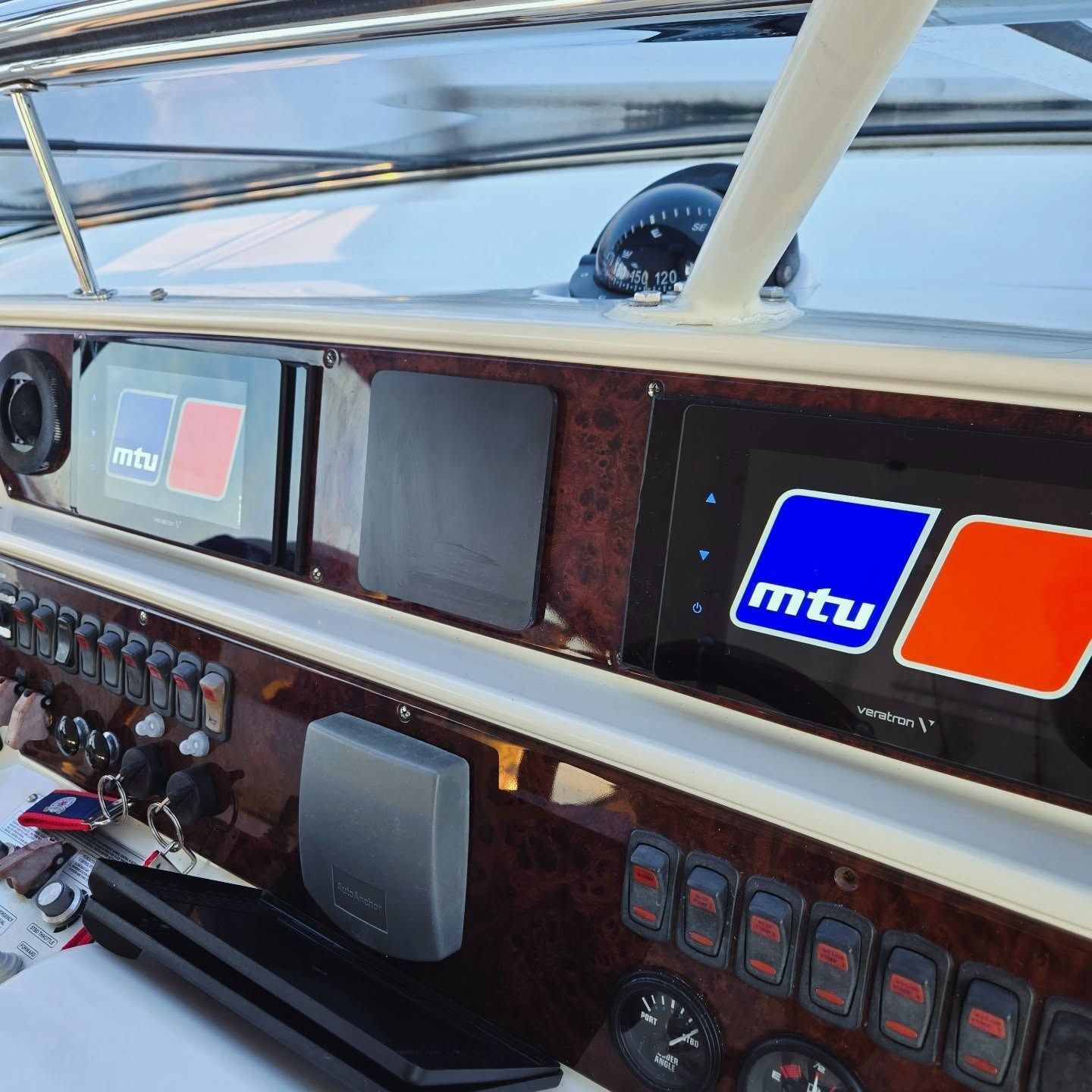 Close-up of a boat cockpit dashboard featuring two MTU digital displays, toggle switches, and a compass.