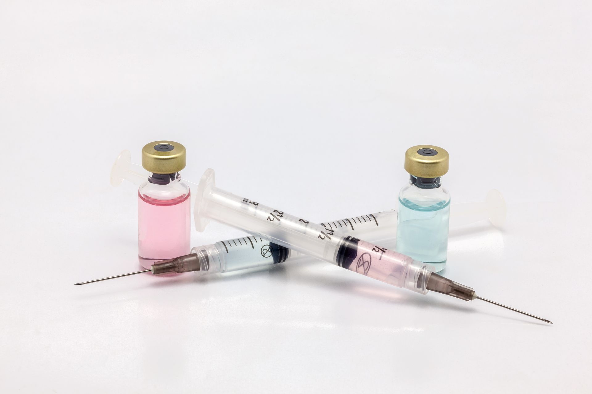 Two syringes and two bottles of liquid on a white surface.