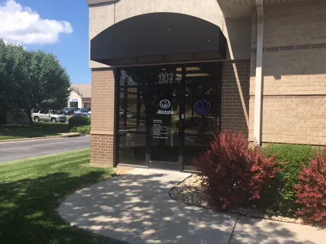 Office building entrance with glass doors, brick facade, and red shrubs by the walkway