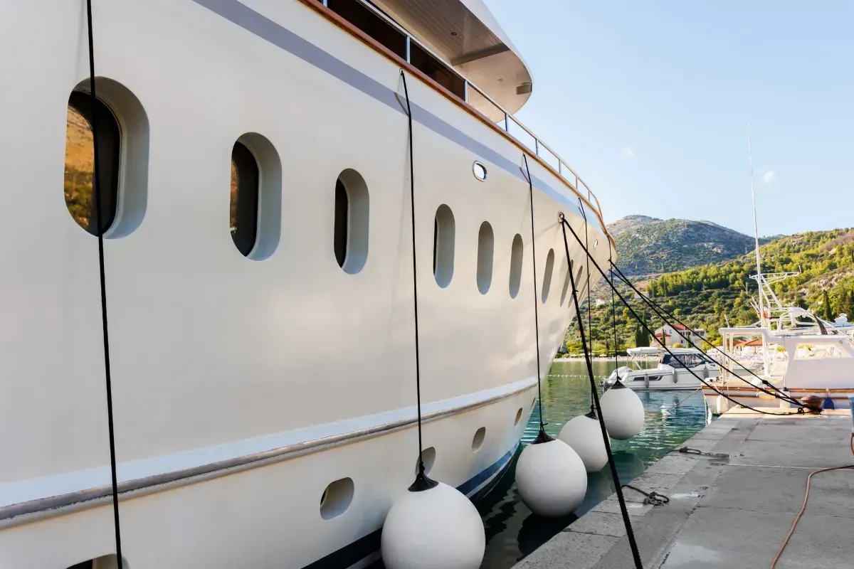 Large white yacht docked at a marina beside a stone walkway and moored boats
