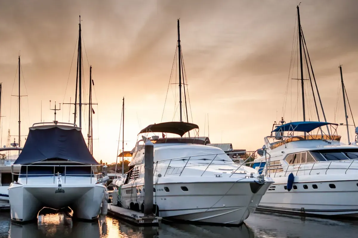 Three yachts docked at a marina at sunset, with warm orange sky reflecting on the water.