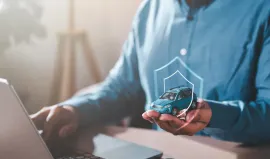 Person using a laptop and holding a small smart home device with a security icon overlay