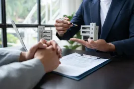Business meeting with hands gesturing over contract documents and two architectural model buildings on a desk