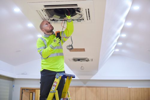 A Man Is Standing On A Ladder Working On A Ceiling Fan - Maricopa, AZ - Eco Mechanical LLC