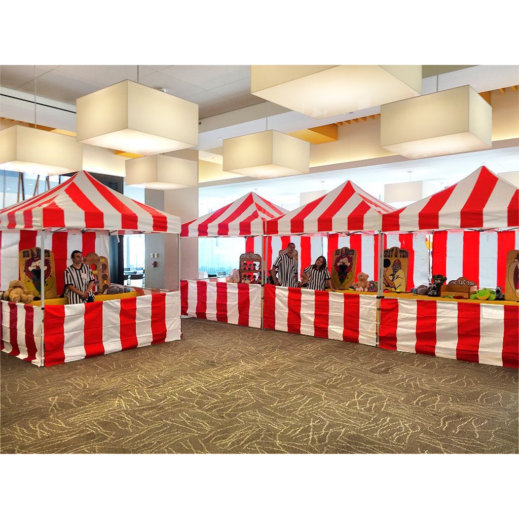 Red and white carnival tents set up indoors, featuring classic midway games and staff.