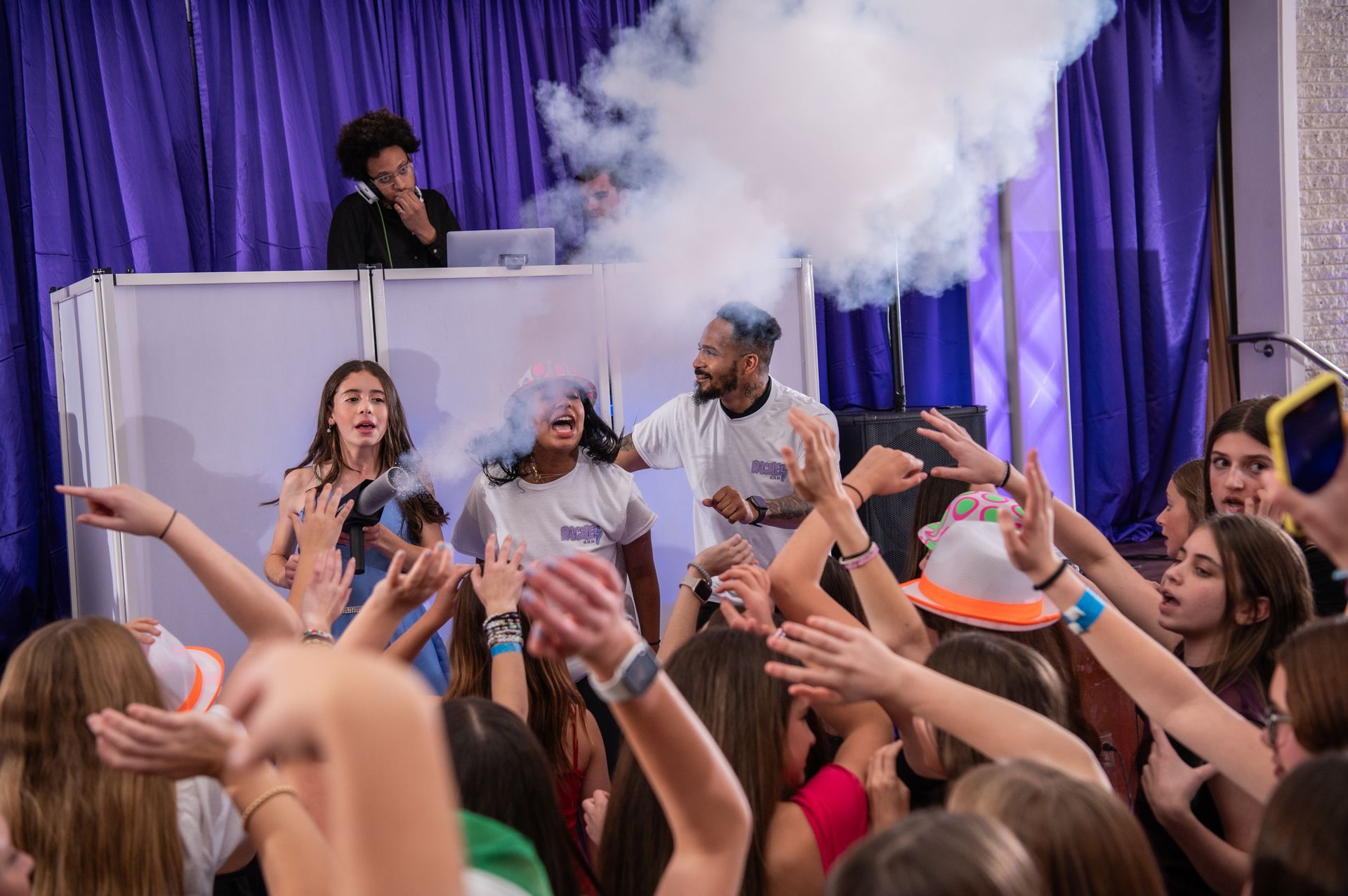 A crowd of people are standing in front of a dj at a party.