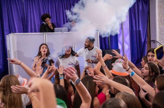 A crowd of people are standing in front of a dj at a party.