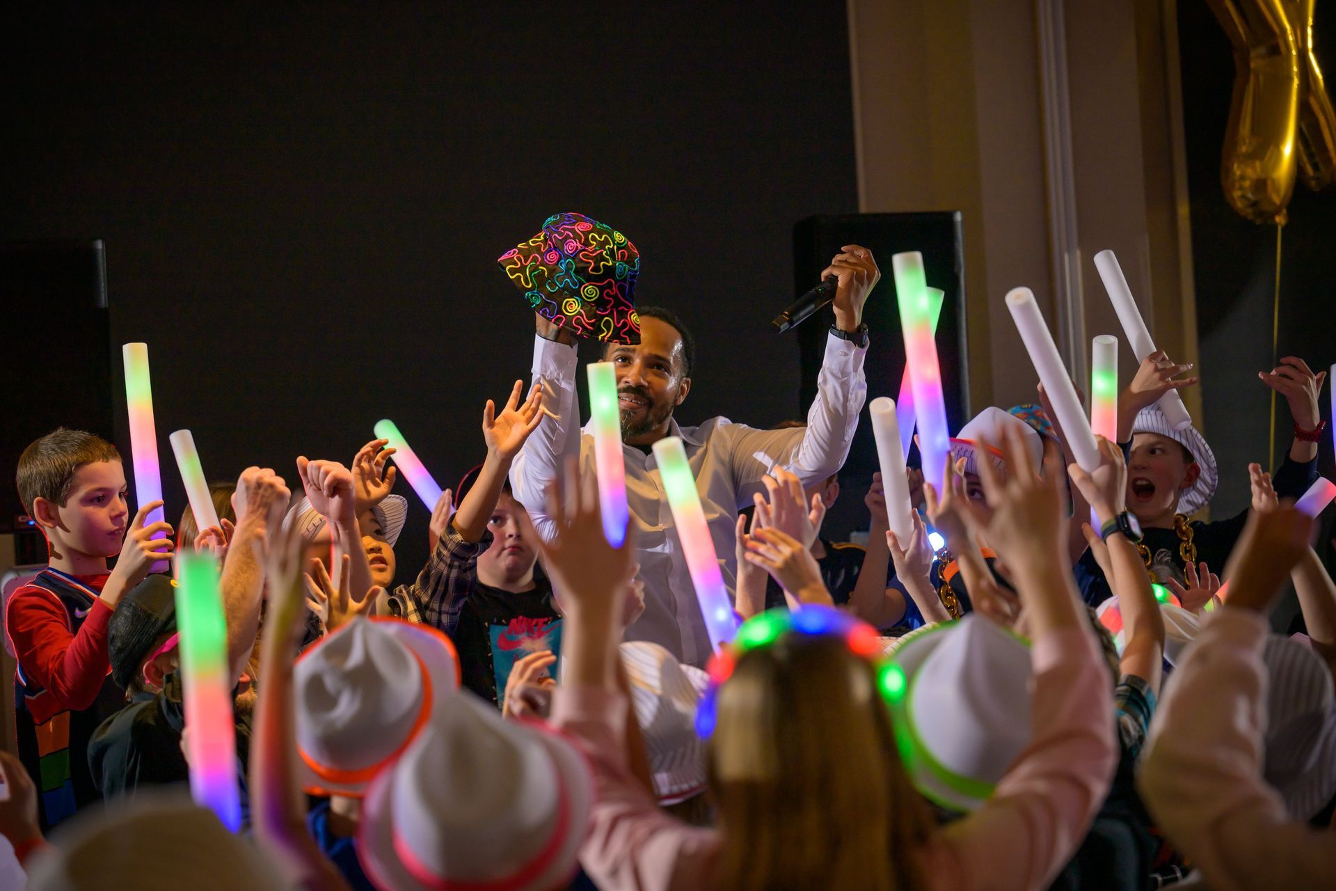A person holds a microphone and a colorful floral bouquet while surrounded by a crowd waving glowing LED light sticks.