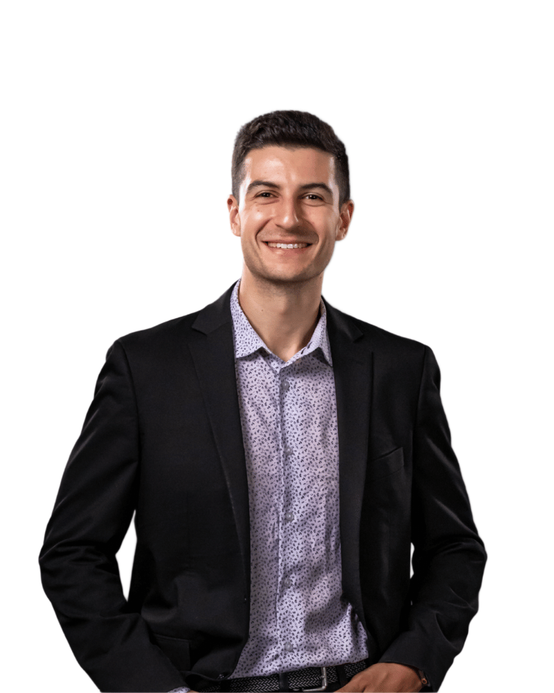 A person wearing a patterned dress shirt and a black blazer against a plain background.
