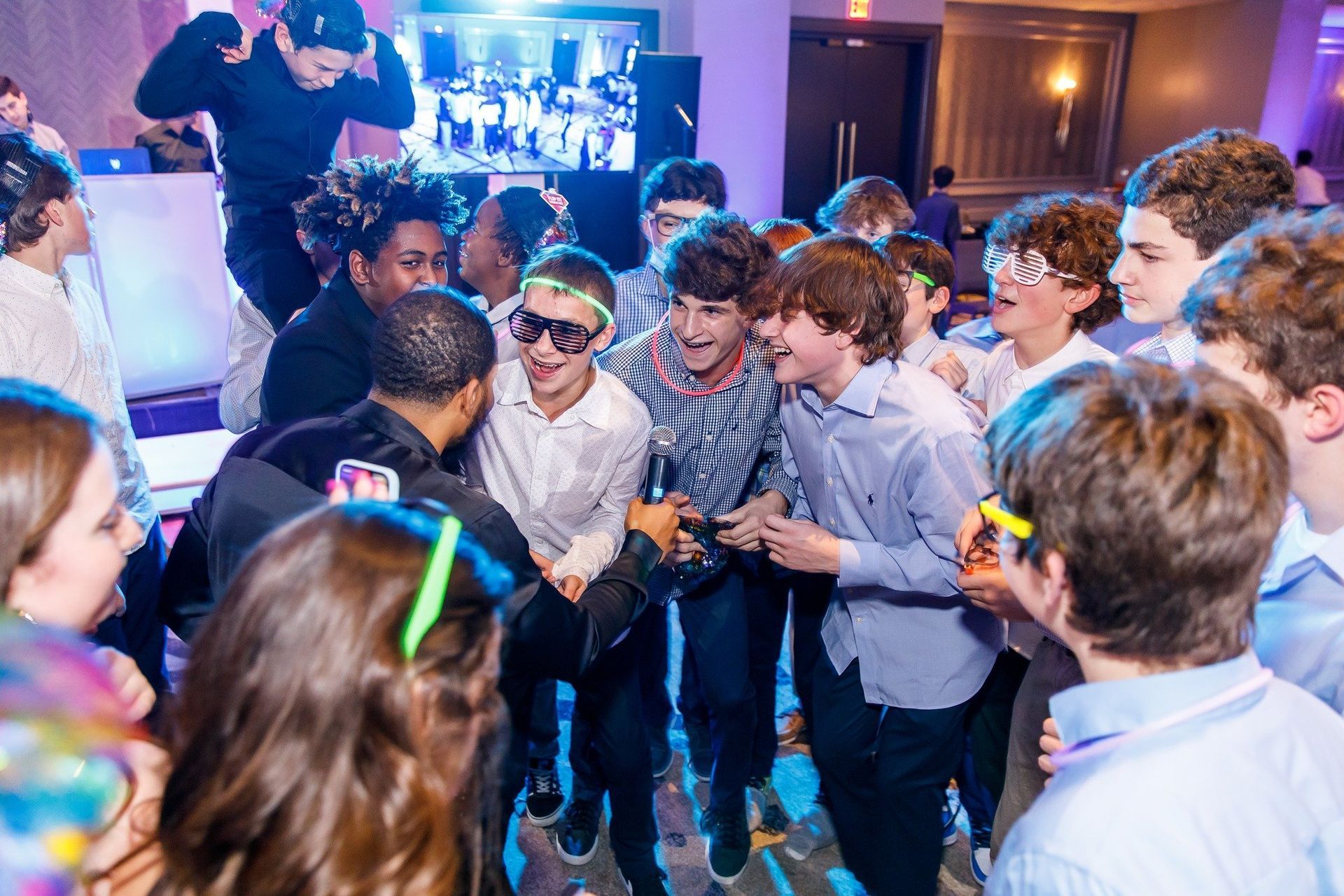 A large group of people celebrating at a party with indoor lighting, colorful glow sticks, and an upbeat atmosphere.