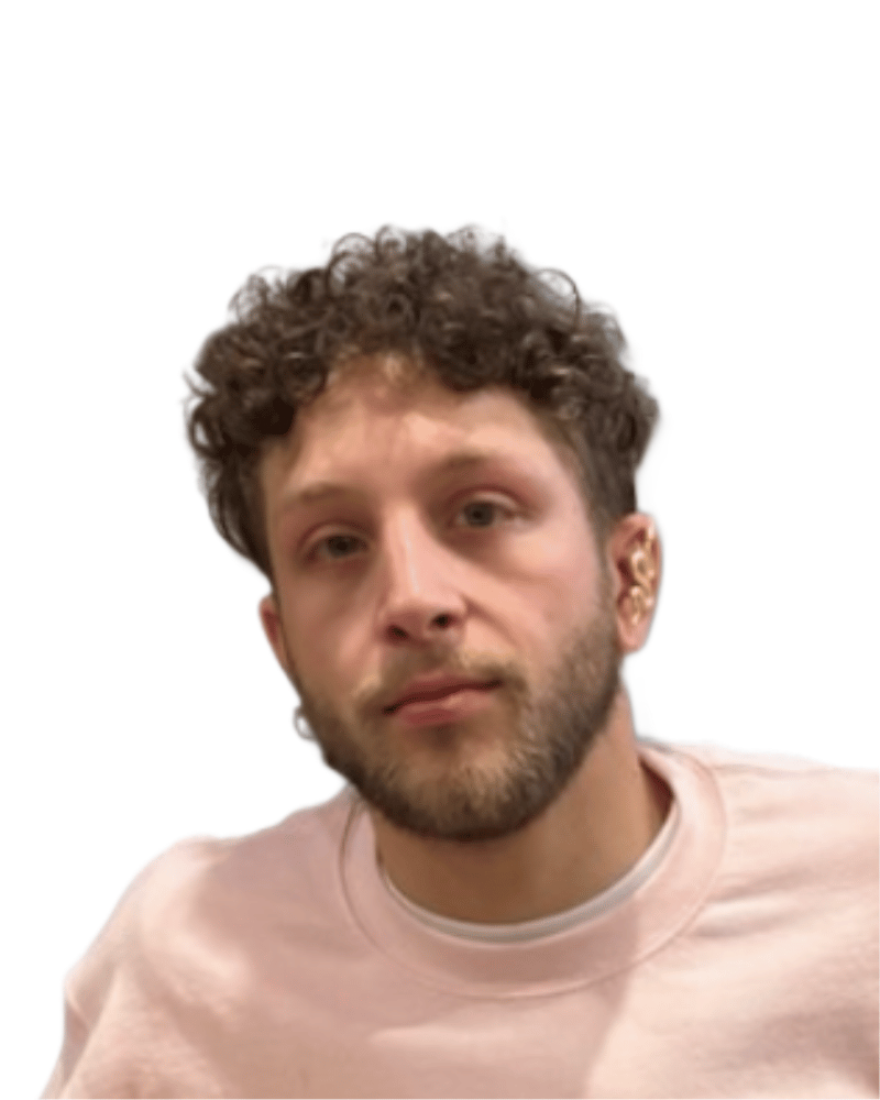A person with curly hair and a beard, wearing a light pink shirt.