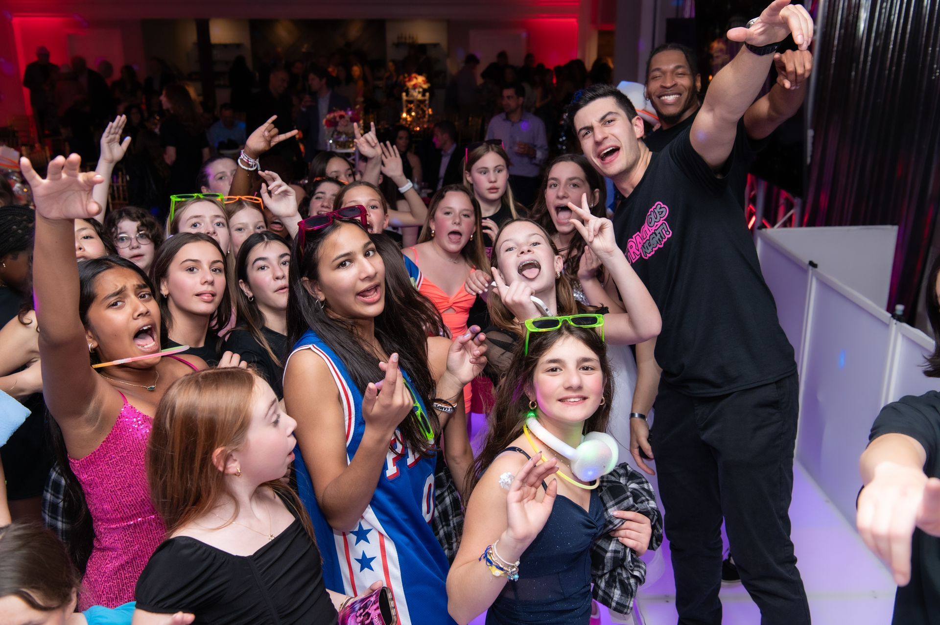 Guests celebrating and dancing at a Mitzvah party with a DJ, vibrant lighting, and entertainment creating a fun atmosphere.