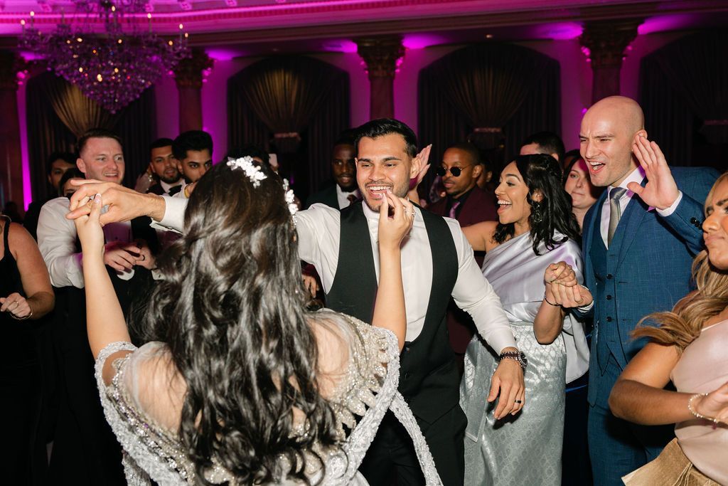 Packed wedding dance floor under magenta lighting and crystal chandeliers