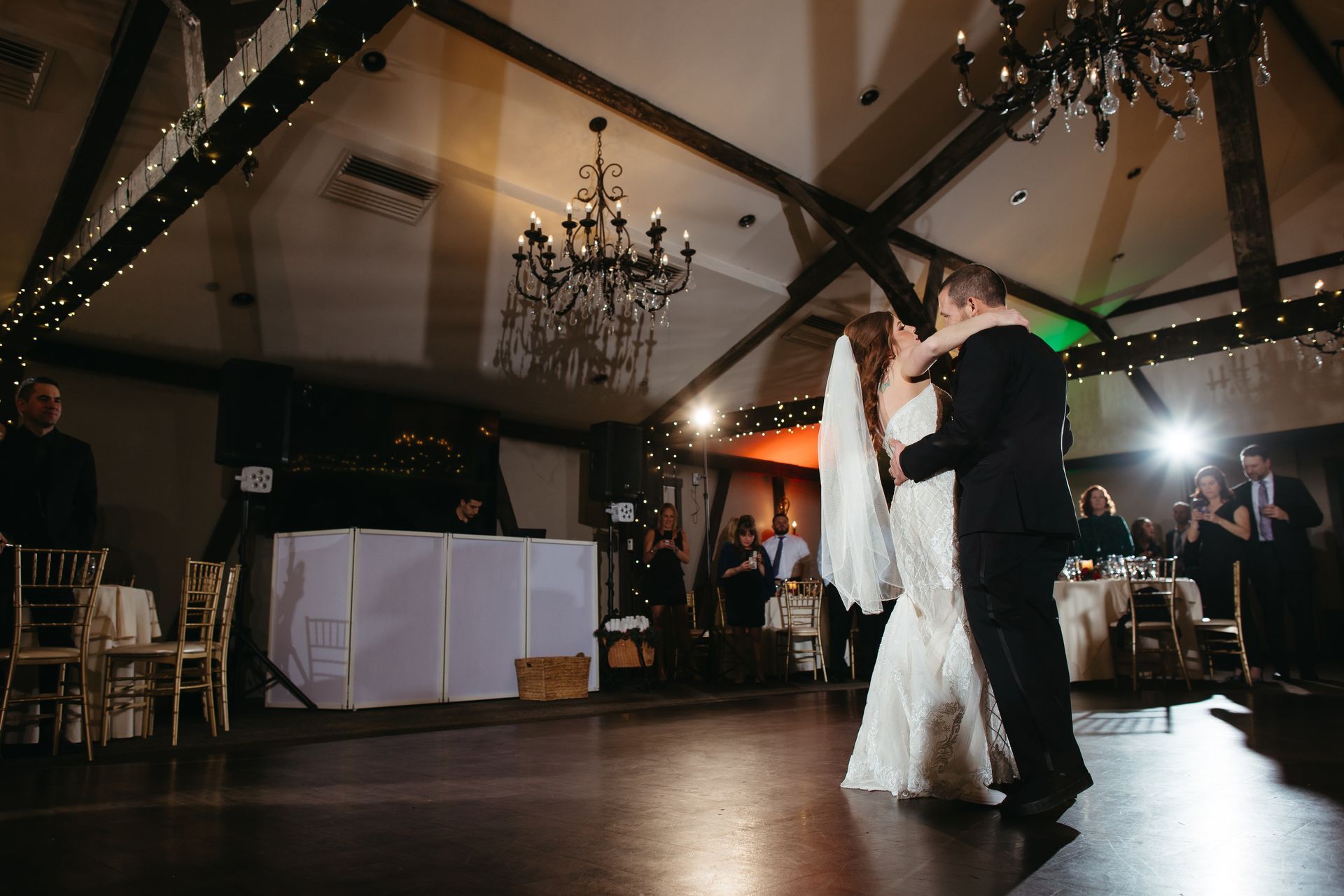 Bride and groom’s first dance beside a white DJ booth under a spotlight and string lights