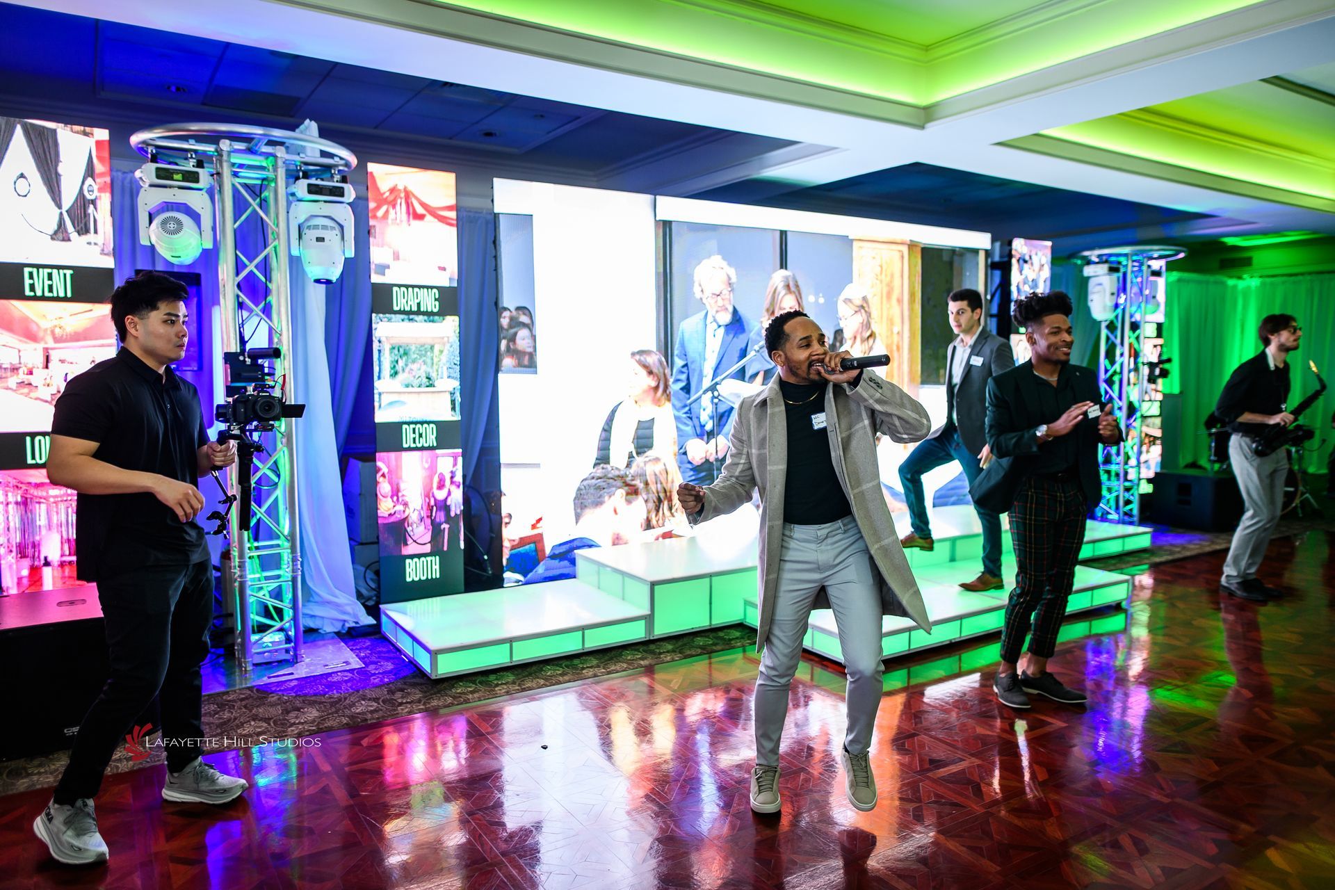 MC on lit LED stage risers with truss lights, LED video walls and green uplighting