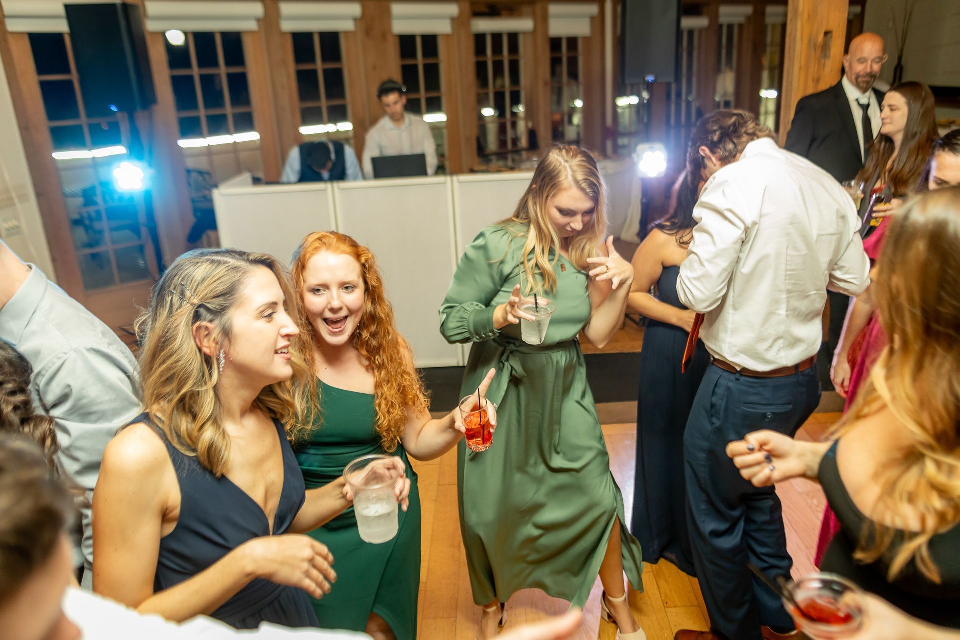 People dancing at a party, a DJ in the background. Wooden beams, various colors, expressions of joy.