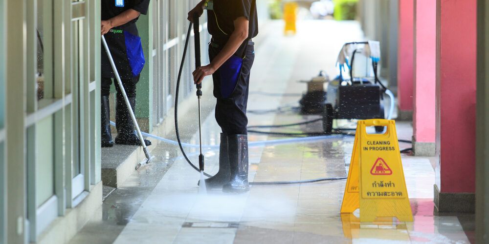 A man is cleaning the floor of a building with a high pressure washer.
