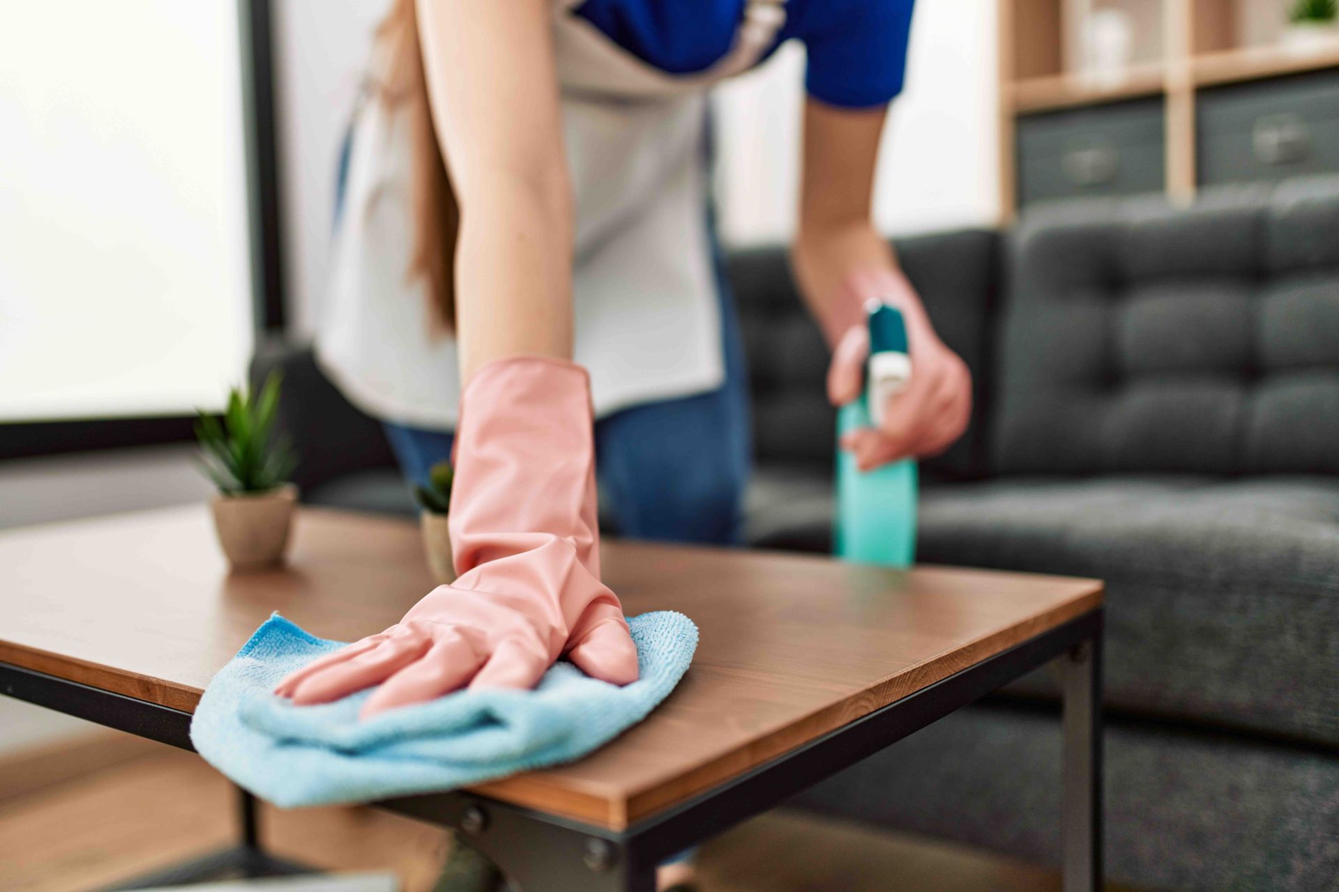 A woman wearing pink gloves is cleaning a wooden table in a living room.