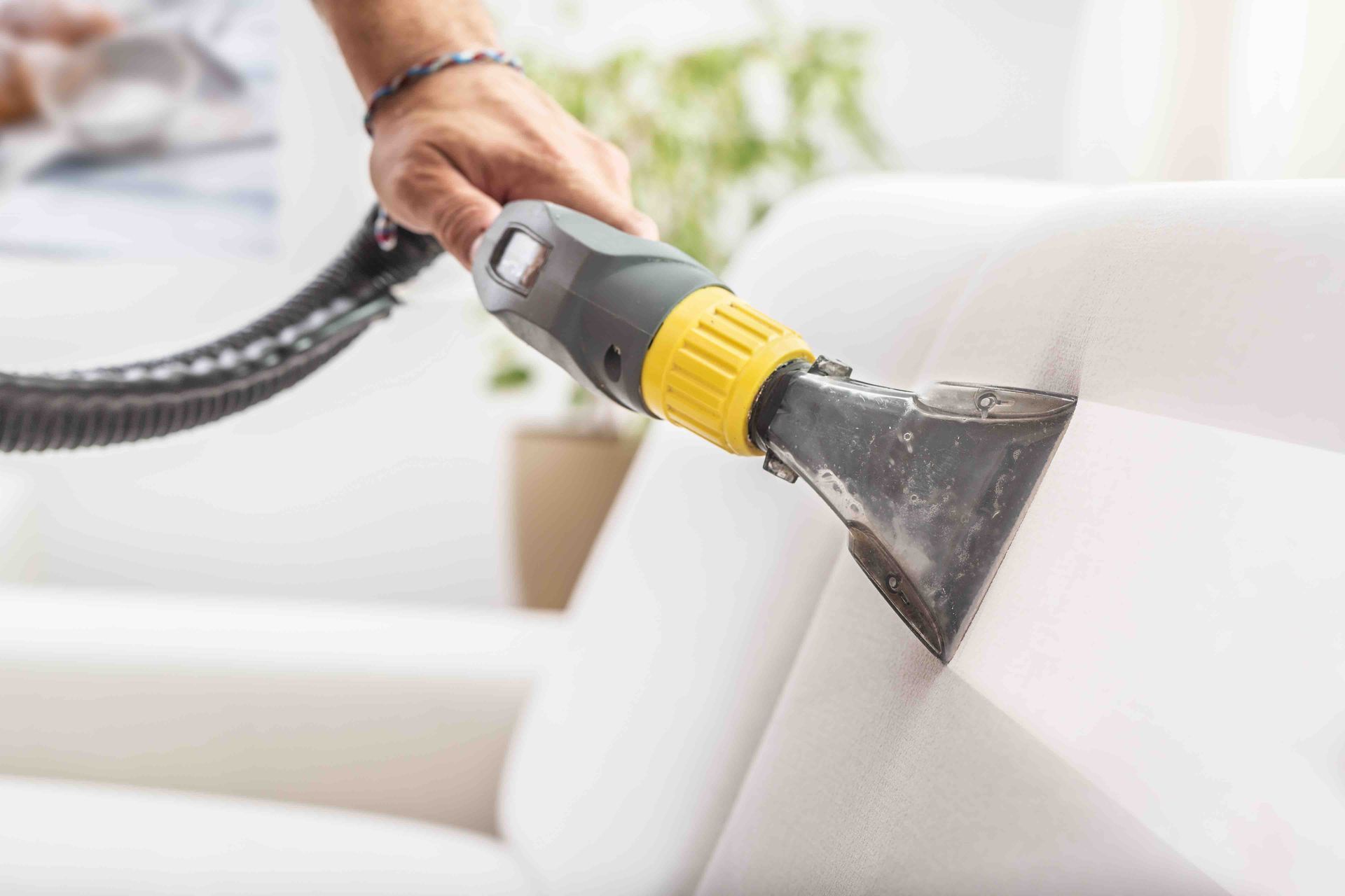A person is cleaning a couch with a vacuum cleaner.