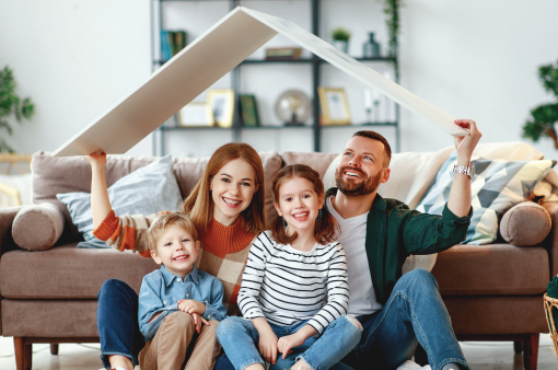 Family sitting on the floor in a living room, smiling while holding a house-shaped frame