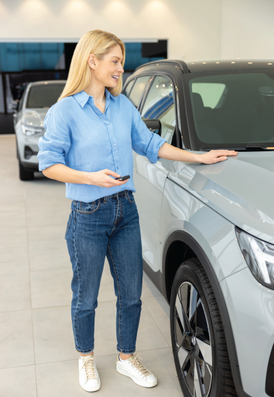 Woman in a blue shirt and jeans standing beside a silver car in a showroom