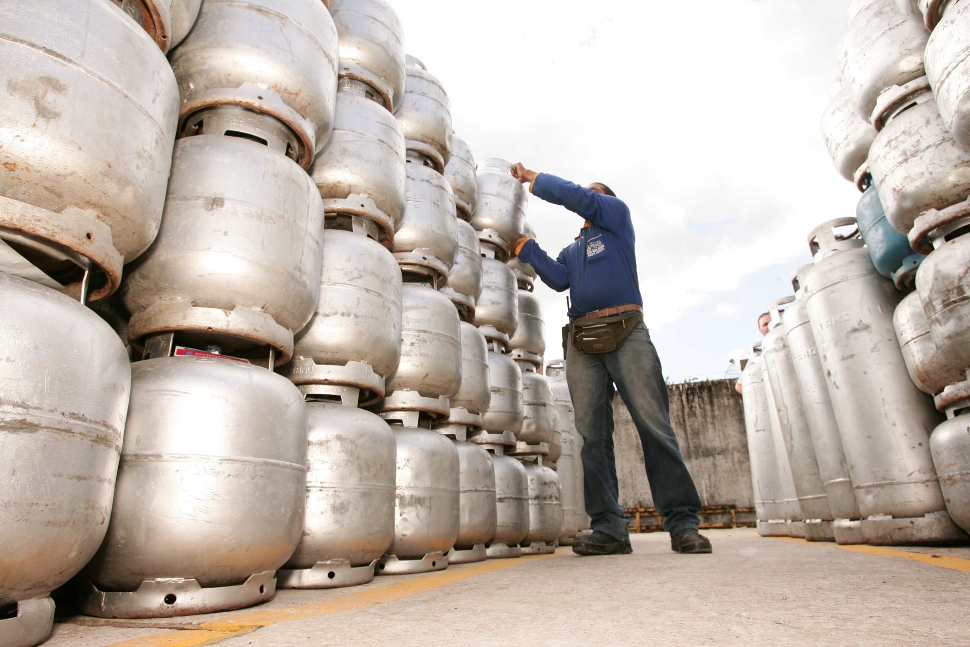 A worker in a blue jacket stacks tall rows of silver cylinders in an outdoor propane delivery yard.